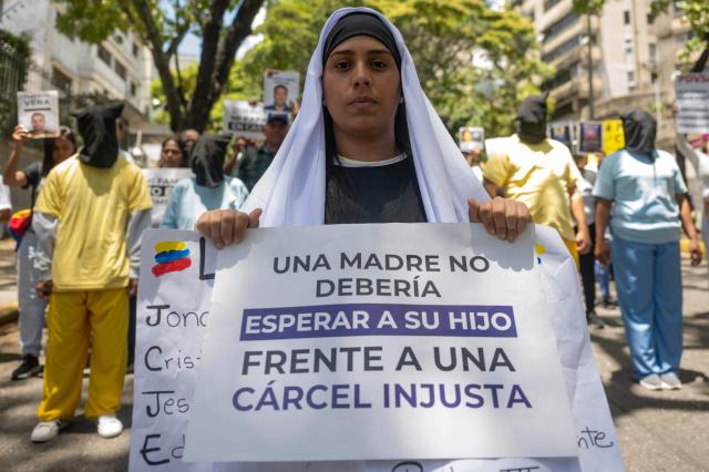 A participant holds a sign reading "A mother should not have to wait for her child in front of an unjust prison" during a march in Caracas on March 27, 2026. Dressed in black and white robes, mothers of political prisoners marched on Friday in Caracas to the headquarters of the nunciature to ask the Vatican to intercede for an amnesty for their relatives. (Photo by Maryorin Mendez / AFP)