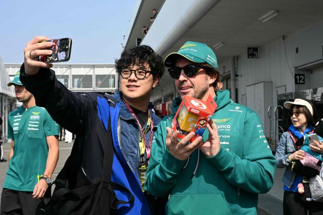 Aston Martin's Spanish driver Fernando Alonso poses with a fan after receiving a gift from him prior to the third practice session ahead of the Formula One Japanese Grand Prix at the Suzuka circuit in Suzuka, Mie prefecture on March 28, 2026. (Photo by Toshifumi KITAMURA / AFP)