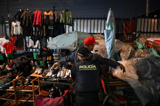 A Colombian police officer searches a man during a patrol in the San Bernardo neighborhood, a critical, high-risk zone known for micro-trafficking, insecurity, and social conflict in downtown Bogota on March 26, 2026. Colombian police use an artificial intelligence tool to predict crime hotspots in real time and create security plans based on large amounts of geographic data. The software, called "IAPol," shows on a map the areas where different risk factors come together, like crime statistics, emergency calls, and police presence, allowing for quicker planning in a country with high crime rates. (Photo by Raul ARBOLEDA / AFP)