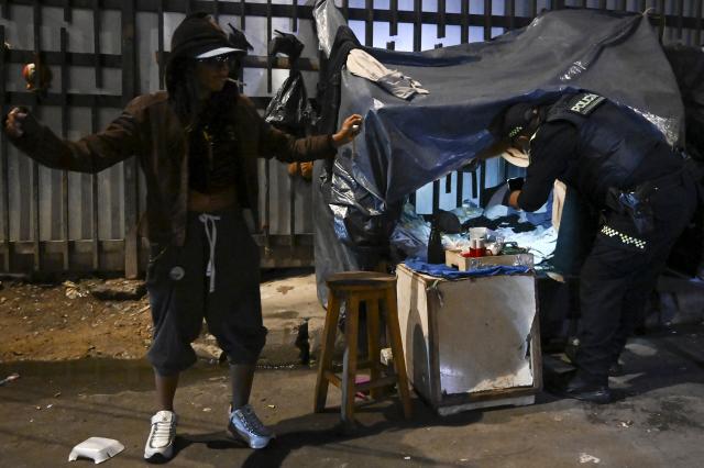 A Colombian police officer searches a man's belongings during a patrol in the San Bernardo neighborhood, a critical, high-risk zone known for micro-trafficking, insecurity, and social conflict in downtown Bogota on March 26, 2026. Colombian police use an artificial intelligence tool to predict crime hotspots in real time and create security plans based on large amounts of geographic data. The software, called "IAPol," shows on a map the areas where different risk factors come together, like crime statistics, emergency calls, and police presence, allowing for quicker planning in a country with high crime rates. (Photo by Raul ARBOLEDA / AFP)