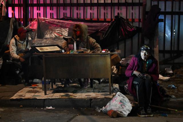 A woman sitting in the street looks on in the San Bernardo neighborhood, a critical, high-risk zone known for micro-trafficking, insecurity, and social conflict in downtown Bogota on March 26, 2026. Colombian police use an artificial intelligence tool to predict crime hotspots in real time and create security plans based on large amounts of geographic data. The software, called "IAPol," shows on a map the areas where different risk factors come together, like crime statistics, emergency calls, and police presence, allowing for quicker planning in a country with high crime rates. (Photo by Raul ARBOLEDA / AFP)