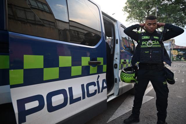 A Colombian police officer prepares to patrol the San Bernardo neighborhood, a critical, high-risk zone known for micro-trafficking, insecurity, and social conflict in downtown Bogota on March 26, 2026. Colombian police use an artificial intelligence tool to predict crime hotspots in real time and create security plans based on large amounts of geographic data. The software, called "IAPol," shows on a map the areas where different risk factors come together, like crime statistics, emergency calls, and police presence, allowing for quicker planning in a country with high crime rates. (Photo by Raul ARBOLEDA / AFP)