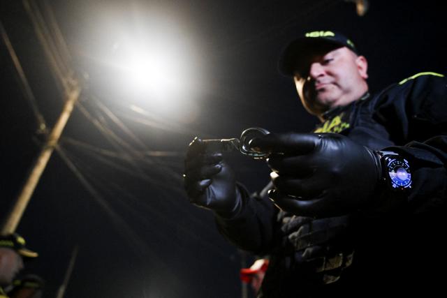 A Colombian police officer holds half of a scissor during a patrol in the San Bernardo neighborhood, a critical, high-risk zone known for micro-trafficking, insecurity, and social conflict in downtown Bogota on March 26, 2026. Colombian police use an artificial intelligence tool to predict crime hotspots in real time and create security plans based on large amounts of geographic data. The software, called "IAPol," shows on a map the areas where different risk factors come together, like crime statistics, emergency calls, and police presence, allowing for quicker planning in a country with high crime rates. (Photo by Raul ARBOLEDA / AFP)