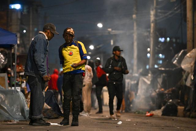 People walk on a street in the San Bernardo neighborhood, a critical, high-risk zone known for micro-trafficking, insecurity, and social conflict in downtown Bogota on March 26, 2026. Colombian police use an artificial intelligence tool to predict crime hotspots in real time and create security plans based on large amounts of geographic data. The software, called "IAPol," shows on a map the areas where different risk factors come together, like crime statistics, emergency calls, and police presence, allowing for quicker planning in a country with high crime rates. (Photo by Raul ARBOLEDA / AFP)
