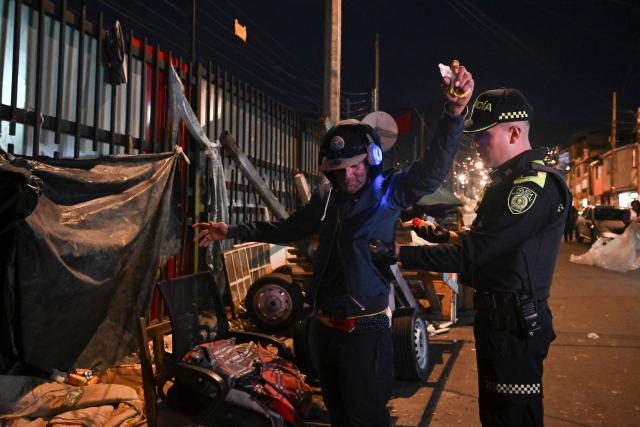 A Colombian police officer searches a man during a patrol in the San Bernardo neighborhood, a critical, high-risk zone known for micro-trafficking, insecurity, and social conflict in downtown Bogota on March 26, 2026. Colombian police use an artificial intelligence tool to predict crime hotspots in real time and create security plans based on large amounts of geographic data. The software, called "IAPol," shows on a map the areas where different risk factors come together, like crime statistics, emergency calls, and police presence, allowing for quicker planning in a country with high crime rates. (Photo by Raul ARBOLEDA / AFP)