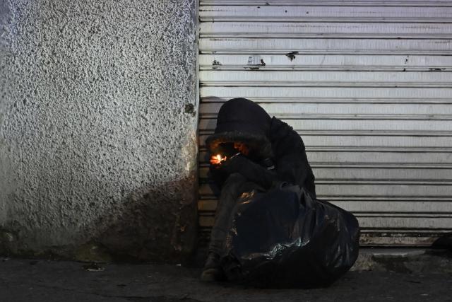 A man lights a pipe in the San Bernardo neighborhood, a critical, high-risk zone known for micro-trafficking, insecurity, and social conflict in downtown Bogota on March 26, 2026. Colombian police use an artificial intelligence tool to predict crime hotspots in real time and create security plans based on large amounts of geographic data. The software, called "IAPol," shows on a map the areas where different risk factors come together, like crime statistics, emergency calls, and police presence, allowing for quicker planning in a country with high crime rates. (Photo by Raul ARBOLEDA / AFP)
