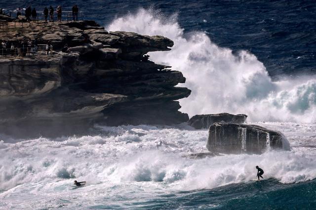 Crowds watch surfers catching large waves breaking at Bondi Beach in Sydney on March 28, 2026 as large swells and high winds create hazardous surf conditions along the south-east coast of Australia. (Photo by DAVID GRAY / AFP)