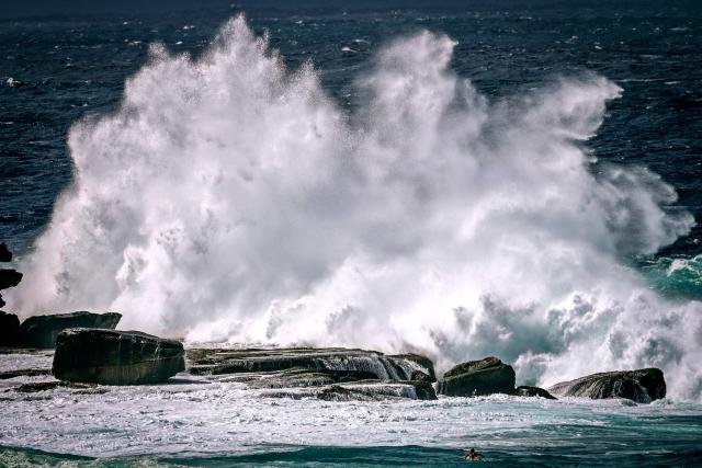 A surfer (R, bottom) paddles towards large waves breaking at Bondi Beach in Sydney on March 28, 2026 as large swells and high winds create hazardous surf conditions along the south-east coast of Australia. (Photo by DAVID GRAY / AFP)