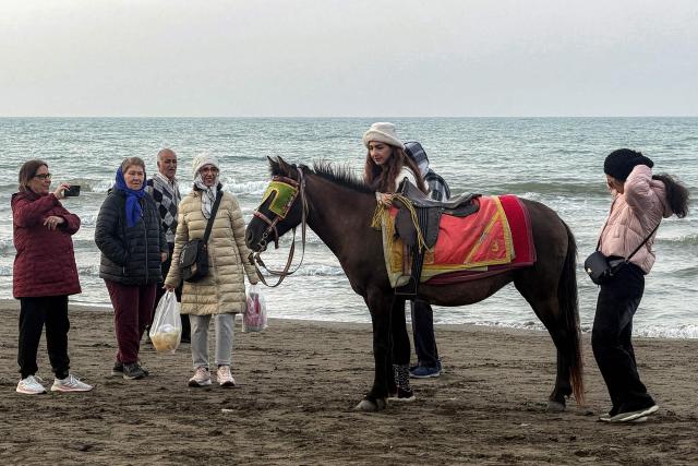 Women stand by a horse waiting along a beach by the Caspian Sea coast in Sorkhrud in Iran's northern Mazandaran province on March 24, 2026, where many families have relocated due to the ongoing war with the US and Israel. Israel and the United States launched strikes on Iran on February 28, killing the Islamic republic's supreme leader and sparking a war that has since spread across the Middle East. (Photo by ATTA KENARE / AFP) / 