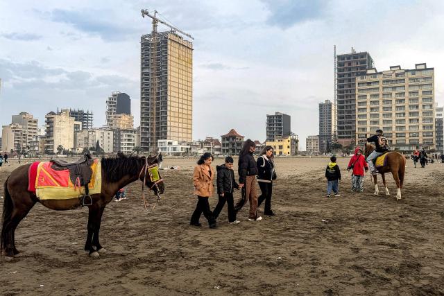 People walk past a horse waiting along a beach by the Caspian Sea coast in Sorkhrud in Iran's northern Mazandaran province on March 24, 2026, where many families have relocated due to the ongoing war with the US and Israel. Israel and the United States launched strikes on Iran on February 28, killing the Islamic republic's supreme leader and sparking a war that has since spread across the Middle East. (Photo by ATTA KENARE / AFP) / 
