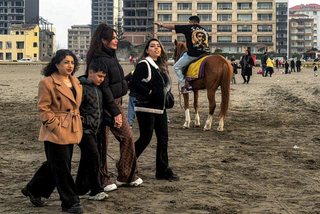 women and a boy walk past a man riding a horse along a beach by the Caspian Sea coast in Sorkhrud in Iran's northern Mazandaran province on March 24, 2026, where many families have relocated due to the ongoing war with the US and Israel. Israel and the United States launched strikes on Iran on February 28, killing the Islamic republic's supreme leader and sparking a war that has since spread across the Middle East. (Photo by ATTA KENARE / AFP) / 