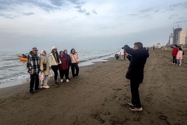 People pose for a picture along a beach by the Caspian Sea coast in Sorkhrud in Iran's northern Mazandaran province on March 24, 2026, where many families have relocated due to the ongoing war with the US and Israel. Israel and the United States launched strikes on Iran on February 28, killing the Islamic republic's supreme leader and sparking a war that has since spread across the Middle East. (Photo by ATTA KENARE / AFP) / 