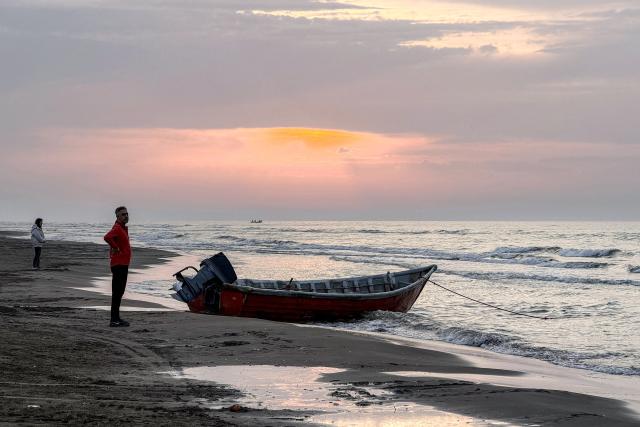 A man stands near a boat moored along a beach on the Caspian Sea coast in Sorkhrud in Iran's northern Mazandaran province on March 24, 2026, where many families have relocated due to the ongoing war with the US and Israel. Israel and the United States launched strikes on Iran on February 28, killing the Islamic republic's supreme leader and sparking a war that has since spread across the Middle East. (Photo by ATTA KENARE / AFP) / 