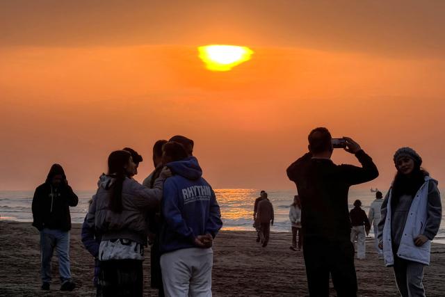 People stand before the setting sun along a beach by the Caspian Sea coast in Sorkhrud in Iran's northern Mazandaran province on March 24, 2026, where many families have relocated due to the ongoing war with the US and Israel. Israel and the United States launched strikes on Iran on February 28, killing the Islamic republic's supreme leader and sparking a war that has since spread across the Middle East. (Photo by ATTA KENARE / AFP) / 