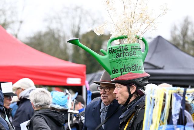A protester has a hat shaped like a watering can during "A water carnaval against Nestle and its world", a protest action called by environmental protection organisations against Nestle Waters in Nancy on March 28, 2026. The Nestle Waters trial over illegal waste dumps in the Vosges department took place from March 23 to 26 in Nancy. The public prosecutor’s office sought a fine of Ђ750,000 – the maximum penalty available – against Nestle Waters Supply Est. (Photo by Jean-Christophe VERHAEGEN / AFP)