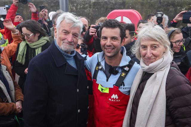 French skipper Guirec Soudйe (C) poses and celebrates with French sailor and former record man Jean-Luc Van Den Heede (L) and France’s junior Minister in charge of the sea and fisheries Catherine Chabaud after beating the record for sailing around the world from east to west, in Brest on March 28, 2026, completing the voyage in 94 days, 21 hours, and 58 minutes. (Photo by FRED TANNEAU / AFP)