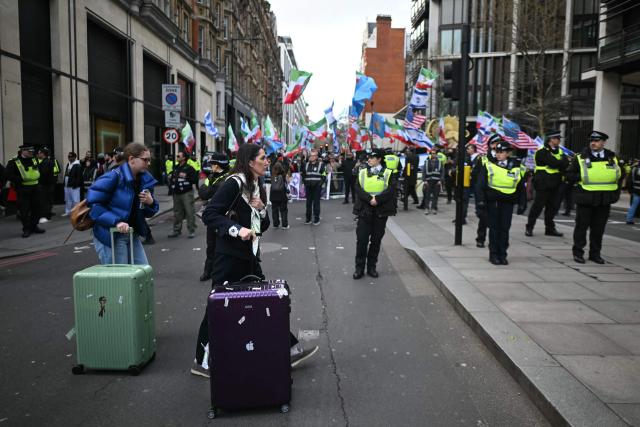 People push suitcases past counter-protesters waving US, Israeli and pre-revolution Iranian flags as a pro-palestinian march organised by the Palestine Coalition passes by, in central London on March 28, 2026.  (Photo by JUSTIN TALLIS / AFP)