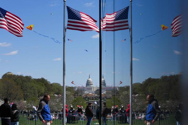 TOPSHOT - People walk near the base of the Washington Monument as kites fly along the National Mall during the Cherry Blossom Kite Festival in Washington, DC, on March 28, 2026. (Photo by Ken Cedeno / AFP)