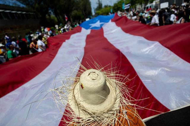 Demonstrators hold a giant flag of Puerto Rico as they march during the "No Kings" national day of protest that included opposition to the proposed Esencia coastal development project in San Juan, Puerto Rico, on March 28, 2026. Nationwide protests against US President Donald Trump are expected Saturday as millions of people vent fury over what they see as his authoritarian bent and other forms of cruel, law-trampling governance. It is the third time in less than a year that Americans will take to the streets as part of a grassroots movement called "No Kings," the most vocal and visual conduit for opposition to Trump since he began his second term in January 2025. (Photo by Ricardo ARDUENGO / AFP)