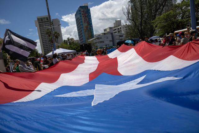 Demonstrators hold a giant flag of Puerto Rico as they march during the "No Kings" national day of protest that included opposition to the proposed Esencia coastal development project in San Juan, Puerto Rico, on March 28, 2026. Nationwide protests against US President Donald Trump are expected Saturday as millions of people vent fury over what they see as his authoritarian bent and other forms of cruel, law-trampling governance. It is the third time in less than a year that Americans will take to the streets as part of a grassroots movement called "No Kings," the most vocal and visual conduit for opposition to Trump since he began his second term in January 2025. (Photo by Ricardo ARDUENGO / AFP)