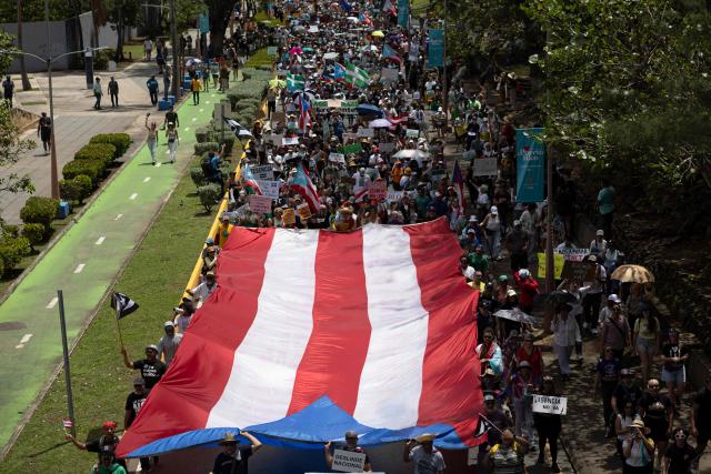 Demonstrators hold a giant flag of Puerto Rico as they march during the "No Kings" national day of protest that included opposition to the proposed Esencia coastal development project in San Juan, Puerto Rico, on March 28, 2026. Nationwide protests against US President Donald Trump are expected Saturday as millions of people vent fury over what they see as his authoritarian bent and other forms of cruel, law-trampling governance. It is the third time in less than a year that Americans will take to the streets as part of a grassroots movement called "No Kings," the most vocal and visual conduit for opposition to Trump since he began his second term in January 2025. (Photo by Ricardo ARDUENGO / AFP)