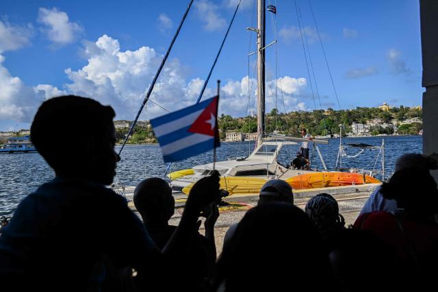 people look on as one of the two sailboats (L) carrying humanitarian aid that had previously gone missing arrives at the port of Havana on March 28, 2026. Two sailboats carrying humanitarian aid to crisis-hit Cuba reached Havana on Saturday after a long journey from Mexico during which they went missing and triggered a search-and-rescue mission. (Photo by Yamil LAGE / AFP)