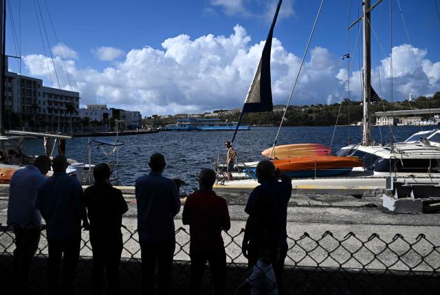 People look on at the two sailboats carrying humanitarian aid, which had previously gone missing, at the port of Havana on March 28, 2026. Two sailboats carrying humanitarian aid to crisis-hit Cuba reached Havana on Saturday after a long journey from Mexico during which they went missing and triggered a search-and-rescue mission. (Photo by Yamil LAGE / AFP)