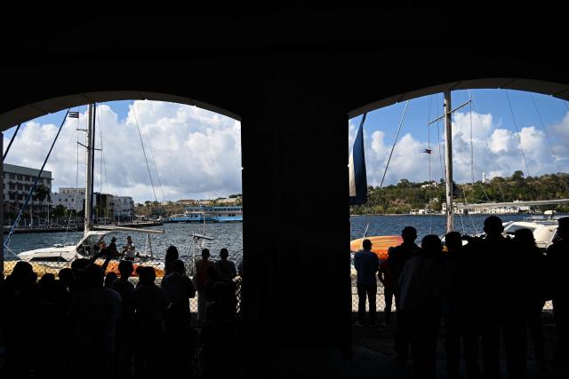 People look on at the two sailboats carrying humanitarian aid, which had previously gone missing, at the port of Havana on March 28, 2026. Two sailboats carrying humanitarian aid to crisis-hit Cuba reached Havana on Saturday after a long journey from Mexico during which they went missing and triggered a search-and-rescue mission. (Photo by Yamil LAGE / AFP)