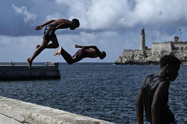 TOPSHOT - Men jump into the sea in the port of Havana on March 28, 2026. (Photo by Yamil LAGE / AFP)