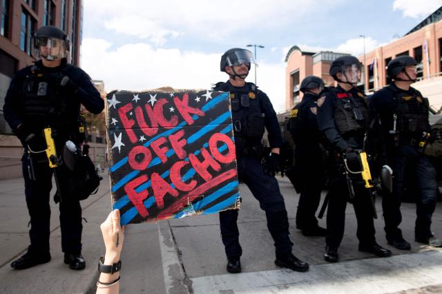 A demonstrator lying on the ground, holds up a sign while facing off with Colorado State Police during the "No Kings" national rally in Denver, Colorado on March 28, 2026. Nationwide protests against US President Donald Trump are expected Saturday as millions of people vent fury over what they see as his authoritarian bent and other forms of cruel, law-trampling governance. It is the third time in less than a year that Americans will take to the streets as part of a grassroots movement called "No Kings," the most vocal and visual conduit for opposition to Trump since he began his second term in January 2025. (Photo by Jason Connolly / AFP)