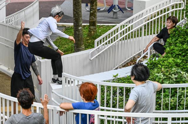This photograph taken on March 17, 2026 shows coach Tan Shie Boon (L) guiding Singaporean elders during a parkour training session in Singapore. This is "geriatric parkour", where around 20 retirees learned to tackle a series of relatively demanding exercises, building their agility and enjoying a sense of camaraderie. (Photo by Roslan RAHMAN / AFP) / To go with "Singapore-Ageism" Focus by Martin ABBUGAO