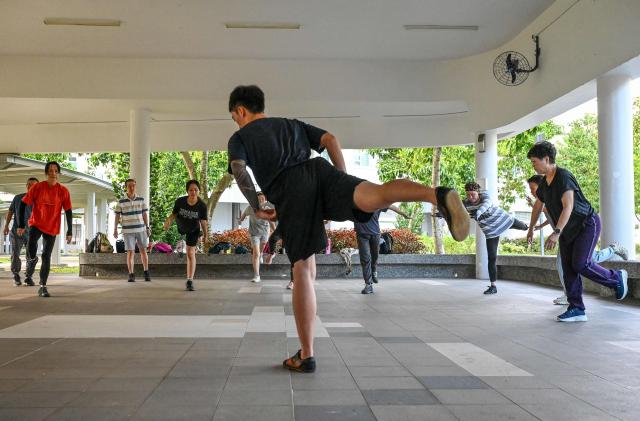 This photograph taken on March 17, 2026 shows coach Tan Shie Boon (C) warming up with Singaporean elders before a parkour training session in Singapore. This is "geriatric parkour", where around 20 retirees learned to tackle a series of relatively demanding exercises, building their agility and enjoying a sense of camaraderie. (Photo by Roslan RAHMAN / AFP) / To go with "Singapore-Ageism" Focus by Martin ABBUGAO