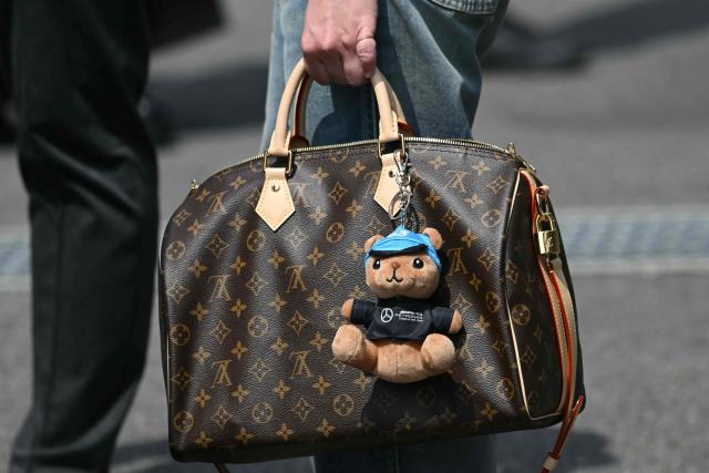 A woman holds a Louis Vuitton bag, seen with a soft toy with the Mercedes logo and the number 63 for Mercedes' British driver George Russel, on race day at the Suzuka circuit during the Formula One Japanese Grand Prix in Suzuka, Mie prefecture on March 29, 2026. (Photo by ANDREW CABALLERO-REYNOLDS / AFP)