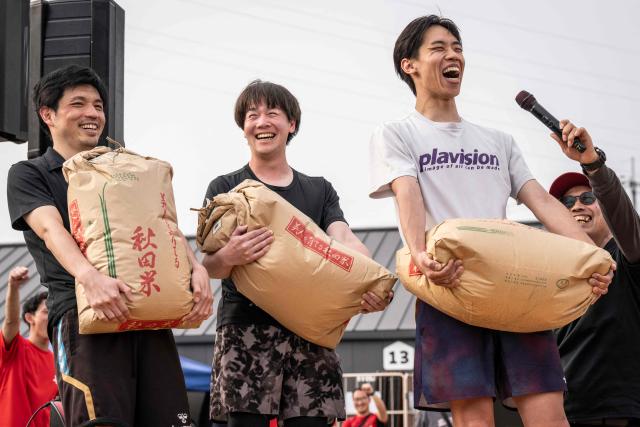 Winner celebrate on the stage as they hold bags of rice as the championship prize, in the ISU-1 Grand Prix in Kyotanabe, Kyoto prefecture on March 29, 2026. The ISU-1 Grand Prix is an endurance race supervised by the Japan Office Chair Racing Association (JORA), in which participants compete to see how many laps they can complete on office chairs over two hours. The event originated in 2010 in the Kirara shopping district of Kyotanabe, Kyoto Prefecture, and is now held at more than 20 locations across Japan. (Photo by Yuichi YAMAZAKI / AFP)