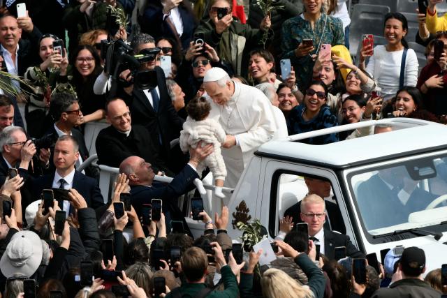 Pope Leo XIV greets a toddler as he leaves after the Palm Sunday mass at St Peter's square in the Vatican on March 29, 2026. (Photo by Marco BERTORELLO / AFP)