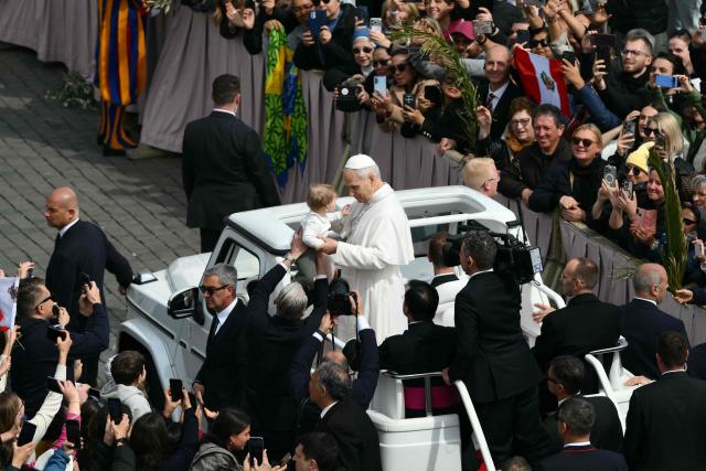 Pope Leo XIV greets a toddler as he leaves after the Palm Sunday mass at St Peter's square in the Vatican on March 29, 2026. (Photo by Marco BERTORELLO / AFP)