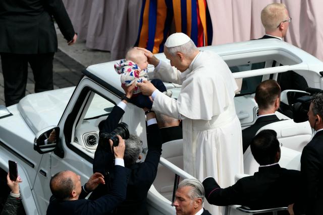 Pope Leo XIV greets a toddler as he leaves after the Palm Sunday mass at St Peter's square in the Vatican on March 29, 2026. (Photo by Marco BERTORELLO / AFP)