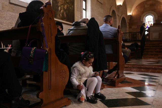 A girl sits with a smartphone as Christian worshippers attend a Palm Sunday mass at the Catholic Church of Saint Catherine, in the Nativity Church Complex, in the occupied West Bank city of Bethlehem on March 29, 2026. Israel has been at war since it and the US launched strikes against Iran on February 28, sparking swift retaliation by the Islamic republic which responded with missile attacks across the region. (Photo by HAZEM BADER / AFP)