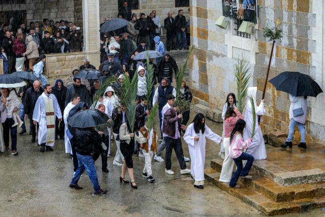Faithful walk through the rain in the procession during the Palm Sunday service at the Maronite Church of Saint George in the southern Lebanese border Christian village of Qlayaa on March 29, 2026. Qlayaa's local parish priest, Father Pierre Rai, was died on March 9 of wounds sustained from Israeli tank fire, sparking anger and fear. Lebanon was drawn into the Middle East war last week when Iran-backed militant group Hezbollah attacked Israel in response to the killing of the Iranian supreme leader during US-Israeli strikes on February 28. (Photo by AFP)