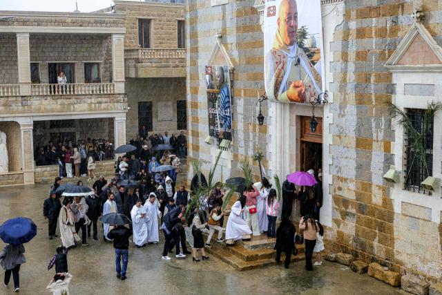 Faithful walk through the rain in the procession during the Palm Sunday service at the Maronite Church of Saint George in the southern Lebanese border Christian village of Qlayaa on March 29, 2026. Qlayaa's local parish priest, Father Pierre Rai, was died on March 9 of wounds sustained from Israeli tank fire, sparking anger and fear. Lebanon was drawn into the Middle East war last week when Iran-backed militant group Hezbollah attacked Israel in response to the killing of the Iranian supreme leader during US-Israeli strikes on February 28. (Photo by AFP)