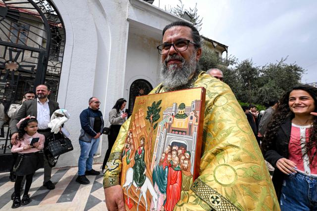 TOPSHOT - A Greek Catholic priest walks with an icon in the procession during the Palm Sunday service at the Cathedral of Our Lady of Dormition, headquarters of the Melkite Patriarchate, in Damascus on March 29, 2026. The Melkite Patriarchate announced on March 28 the cancellation of all its public Easter celebrations in Syria for 2026, citing ongoing security concerns and unstable conditions across the country, to be replaced with scaled-back services limited to prayers held inside churches. (Photo by LOUAI BESHARA / AFP)
