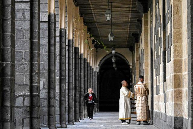 Clergymen stand outside during the Palm Sunday service at the Cathedral of Our Lady of Dormition, headquarters of the Melkite Greek Catholic Patriarchate, in Damascus on March 29, 2026. The Melkite Patriarchate announced on March 28 the cancellation of all its public Easter celebrations in Syria for 2026, citing ongoing security concerns and unstable conditions across the country, to be replaced with scaled-back services limited to prayers held inside churches. (Photo by LOUAI BESHARA / AFP)