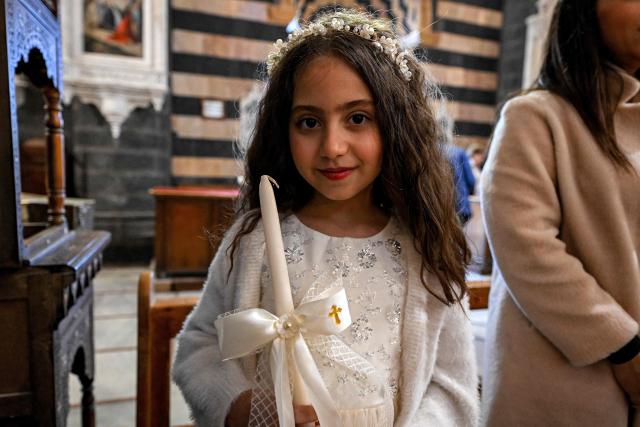 TOPSHOT - A girl stands with an unlit candle during the Palm Sunday service at the Cathedral of Our Lady of Dormition, headquarters of the Melkite Greek Catholic Patriarchate, in Damascus on March 29, 2026. The Melkite Patriarchate announced on March 28 the cancellation of all its public Easter celebrations in Syria for 2026, citing ongoing security concerns and unstable conditions across the country, to be replaced with scaled-back services limited to prayers held inside churches. (Photo by LOUAI BESHARA / AFP)