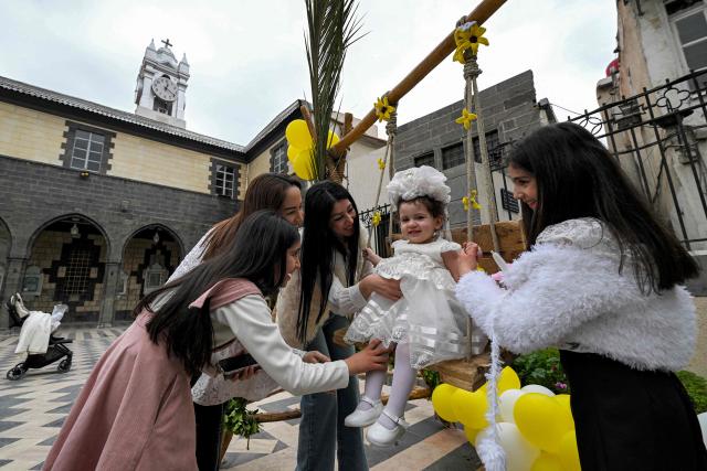 Women help a girl on a swing outside during the Palm Sunday service at the Cathedral of Our Lady of Dormition, headquarters of the Melkite Greek Catholic Patriarchate, in Damascus on March 29, 2026. The Melkite Patriarchate announced on March 28 the cancellation of all its public Easter celebrations in Syria for 2026, citing ongoing security concerns and unstable conditions across the country, to be replaced with scaled-back services limited to prayers held inside churches. (Photo by LOUAI BESHARA / AFP)