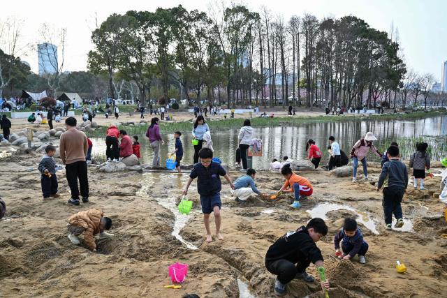 Children play on the sand next to a lake at the Century Park in Shanghai on March 29, 2026. (Photo by Hector RETAMAL / AFP)