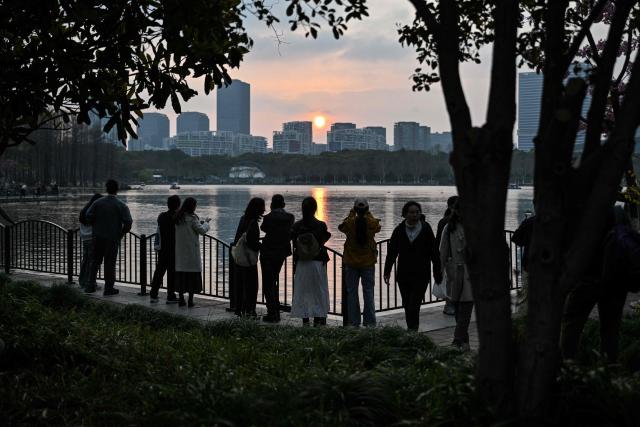 People enjoy sunset at the Century Park in Shanghai on March 29, 2026. (Photo by Hector RETAMAL / AFP)