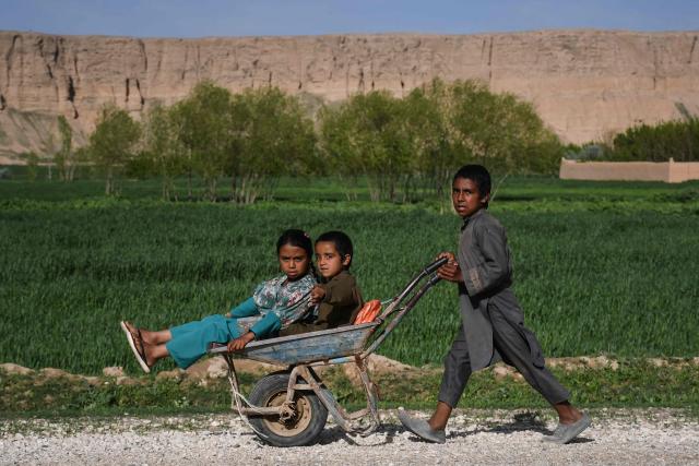 Afghan children ride a wheelbarrow along a roadside at the Paikandara area of Sholgara district in Balkh province on March 29, 2026. (Photo by Atif Aryan / AFP)