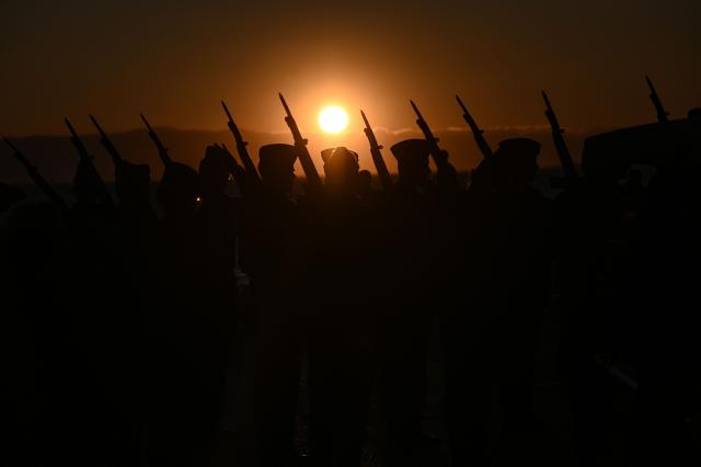 Greek army soldiers stand at attention by the waterfront as the sun sets before the downhaul of the flag at the White Tower in Thessaloniki on March 29, 2026. (Photo by Sakis Mitrolidis / AFP)