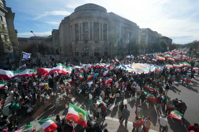 This image taken through a window shows demonstrators waving Iranian pre-1979 Islamic Revolution flags and hold a large banner with an image of Reza Pahlavi, son of the last shah of Iran, as they march toward the White House during a rally in support of Iranians' fight for freedom, in Washington, DC, on March 29, 2026. The event, organized by DCProtests4Iran, brought together members of the Iranian diaspora from the Washington, DC metropolitan area and surrounding states. (Photo by Ken Cedeno / AFP)