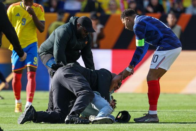 France's forward #10 Kylian Mbappe assists a fan who jumped onto the field to greet him as he's restrained by security at the end of a friendly football match between Colombia and France at Northwest Stadium in Landover, Maryland, on March 29, 2026. (Photo by FRANCK FIFE / AFP)